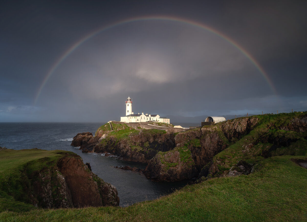 Fanad Head Lighthouse on Donegal’s north coast beneath a full rainbow, with dramatic cliffs, Atlantic Ocean, and stormy skies creating a striking coastal landscape in Ireland.