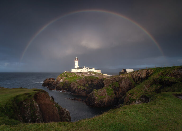 Fanad Head Lighthouse on Donegal’s north coast beneath a full rainbow, with dramatic cliffs, Atlantic Ocean, and stormy skies creating a striking coastal landscape in Ireland.