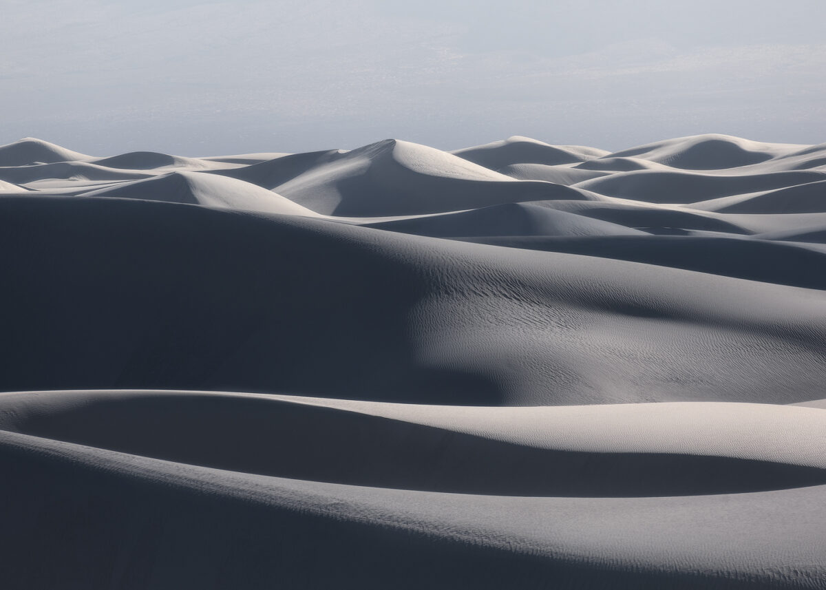 Layers of white gypsum dunes recede into the distance at White Sands National Park, with soft light and deep shadows revealing the sculpted curves of the landscape.
