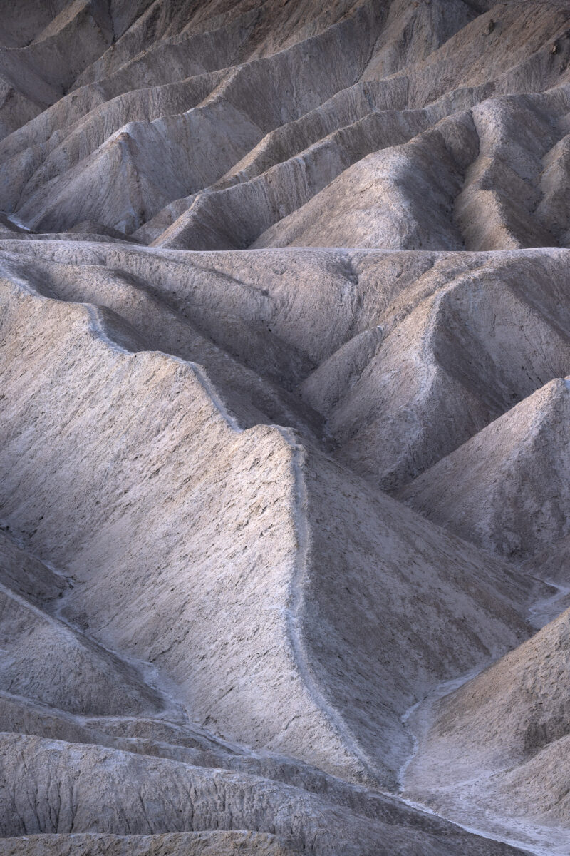 Intricate badland formations carved into pale desert earth, creating a pattern of ridges, gullies and repeating textures.