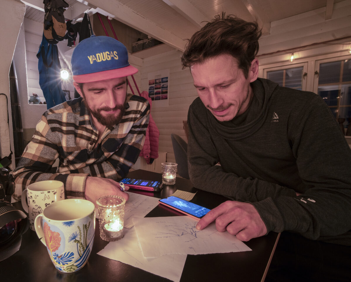 Two photographers reviewing aurora forecasts and location plans around a table in a cozy Arctic cabin.