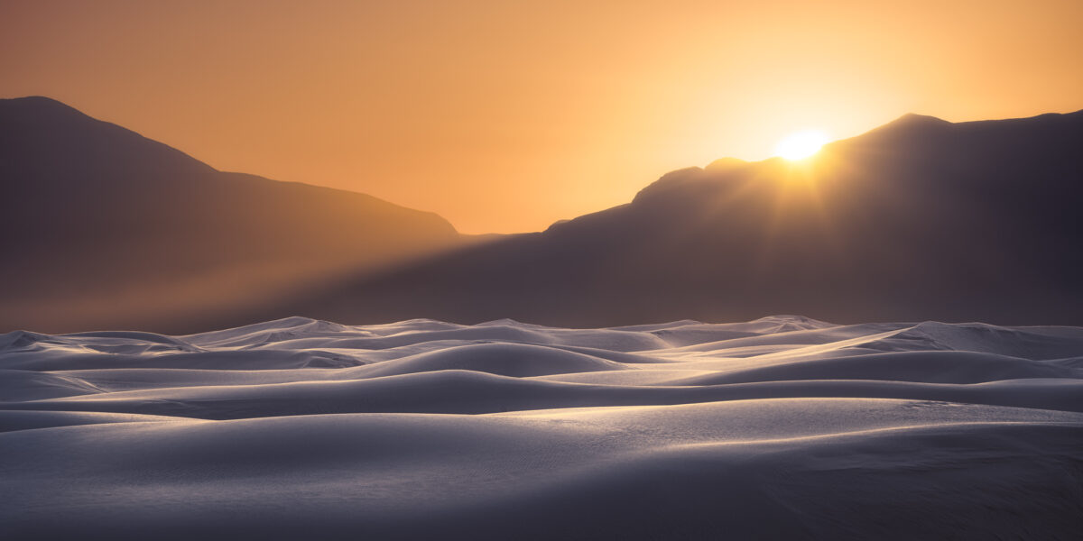 Sunrise over the gypsum dunes of White Sands National Park, with warm golden light illuminating rolling white dunes beneath silhouetted mountains.