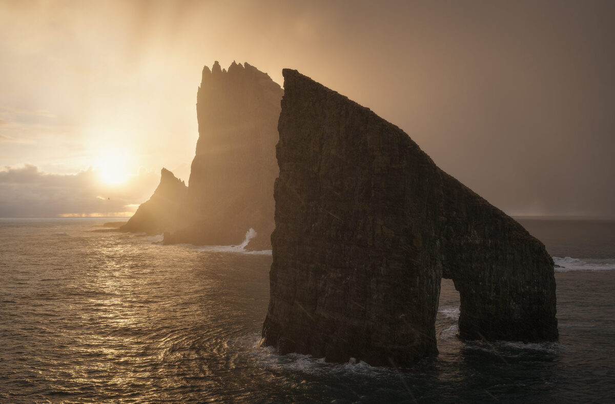 Dramatic sea stacks and jagged cliffs in the Faroe Islands glowing in golden atmospheric sunlight.