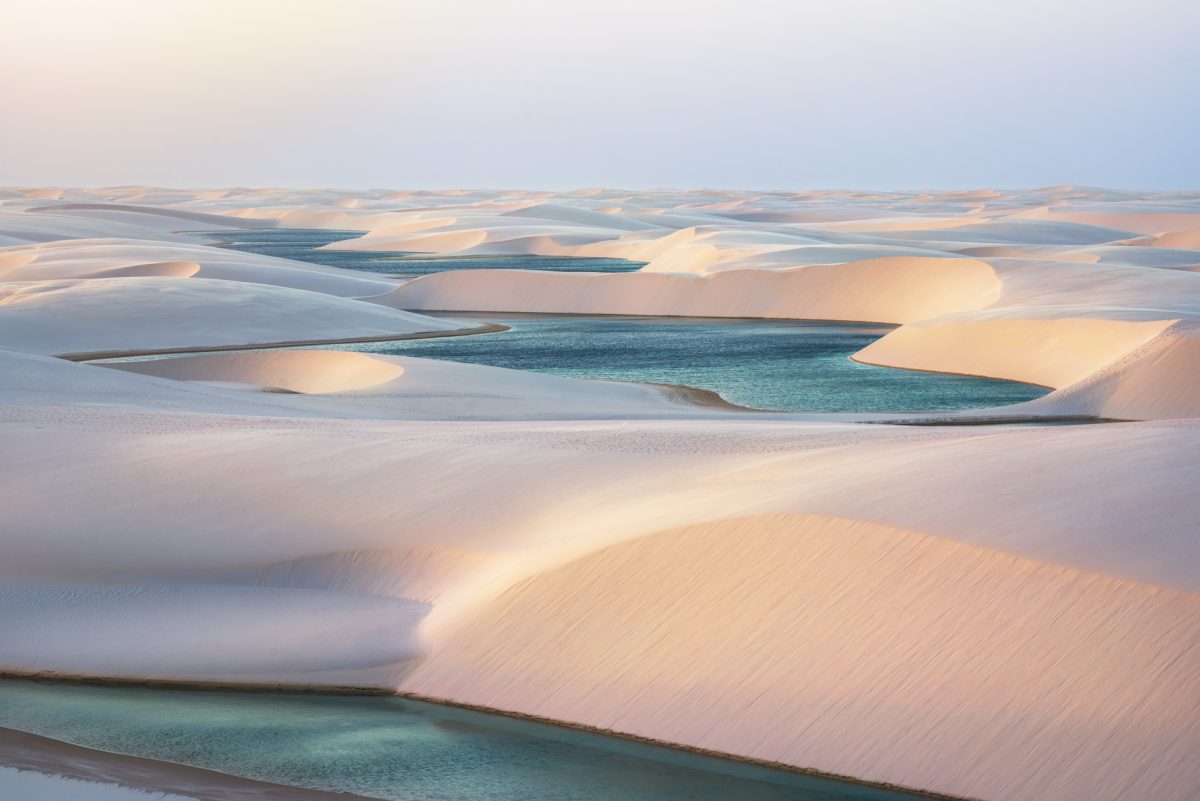 Soft, rolling white sand dunes framing vibrant turquoise lagoons under a gentle twilight sky.