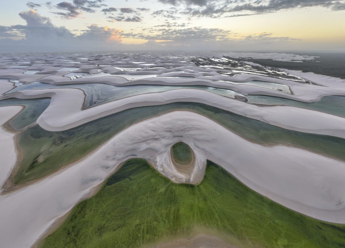 An aerial view of Lençóis Maranhenses showing sweeping white sand dunes intermixed with clear blue and green freshwater lagoons.