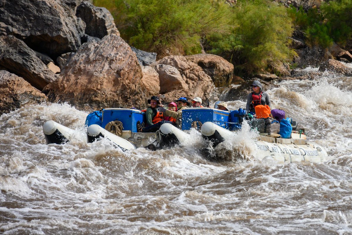 An inflatable raft carrying passengers through turbulent whitewater on the Colorado River in the Grand Canyon.