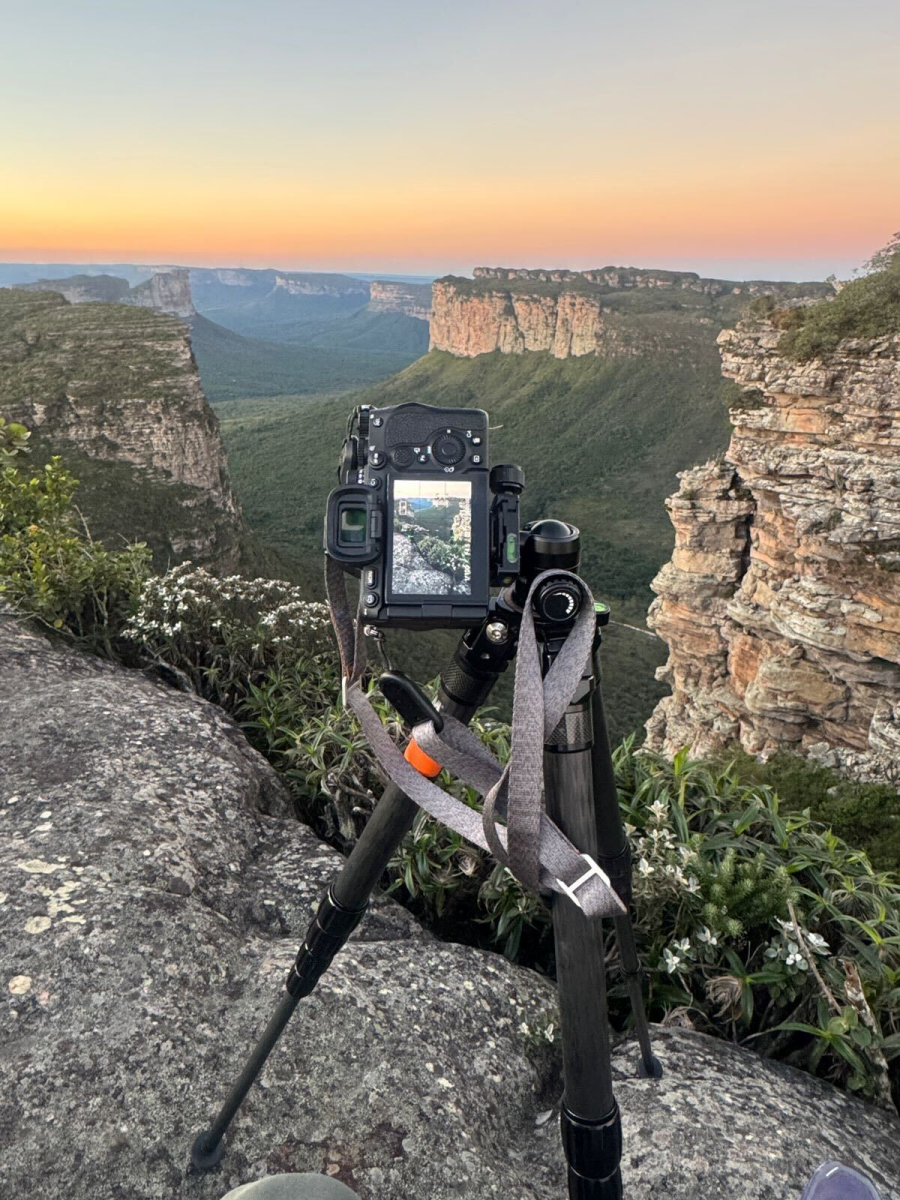 Camera mounted on a tripod overlooking a dramatic canyon landscape at sunset, with layered cliffs and green vegetation stretching into the distance.