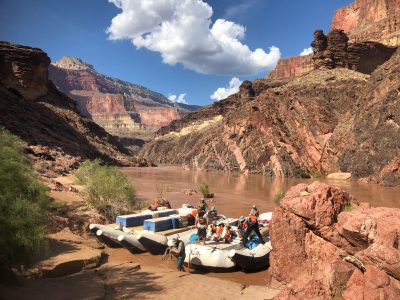 Inflatable rafts pulled up beside the Colorado River beneath towering red and black canyon walls.